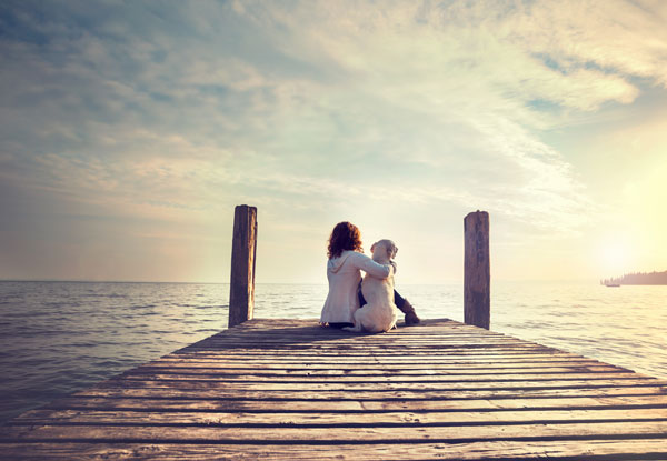 Frau mit Hund blickt hoffnungsvoll zum Horizont der Gesundheit
